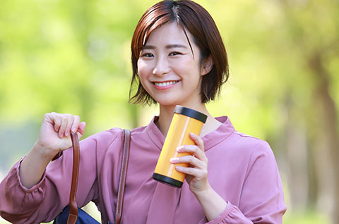 Smiling woman holding yellow travel mug outdoors